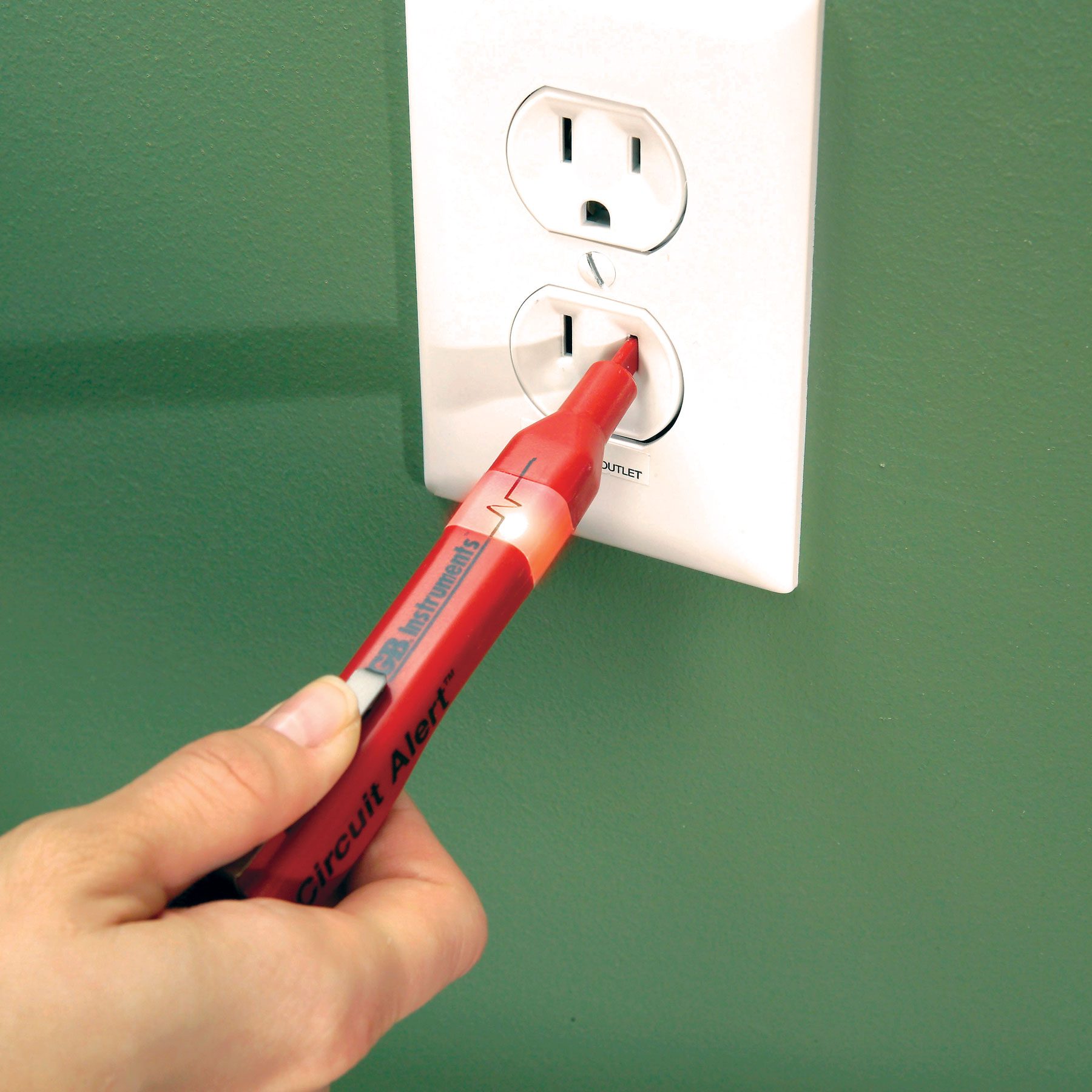 A hand can be seen using a Non-Contact Voltage Tester to test a receptacle.