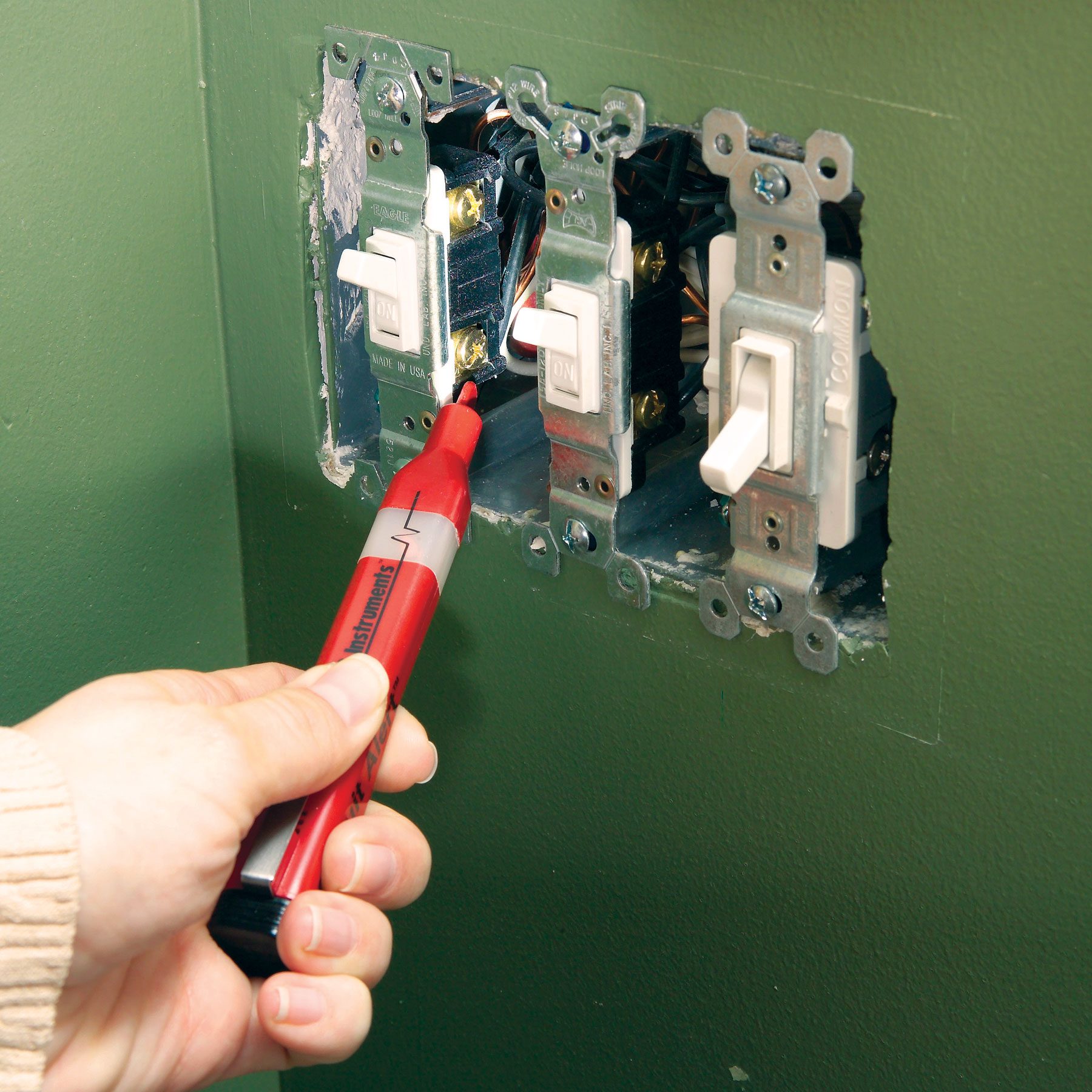 A hand can be seen using a non-contact voltage tester to diagnose a faulty switch.