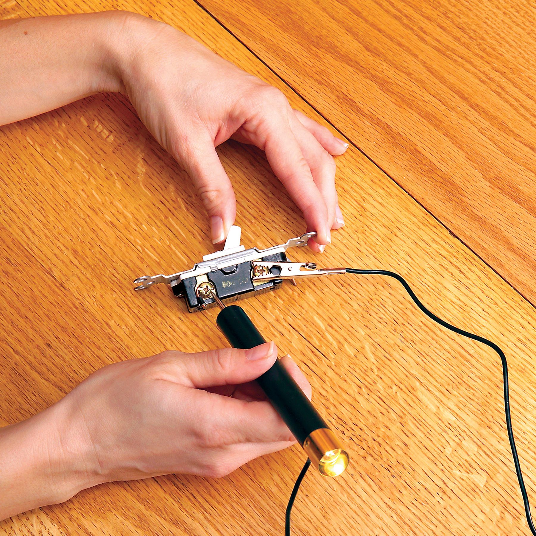 Hands can be seen using a continuity tester to check a switch on a wooden surface.
