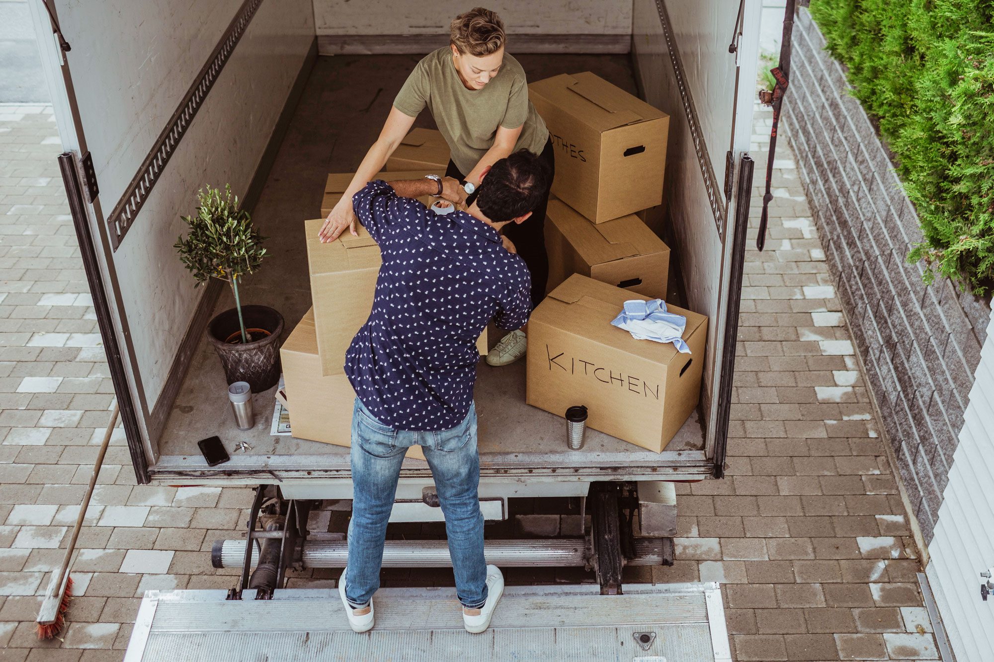 Rear View Of Male Helping Female Carrying Cardboard Boxes Outside Van