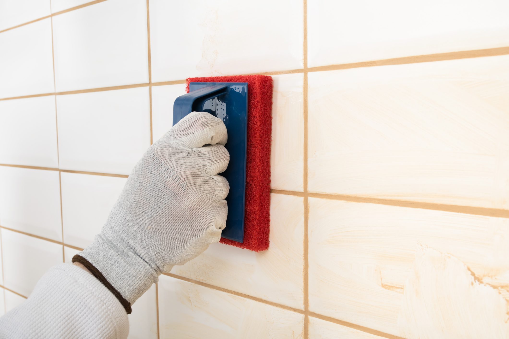 the hands of the master rubs the brown grout on white tiles with a special sponge, finishing work, close-up