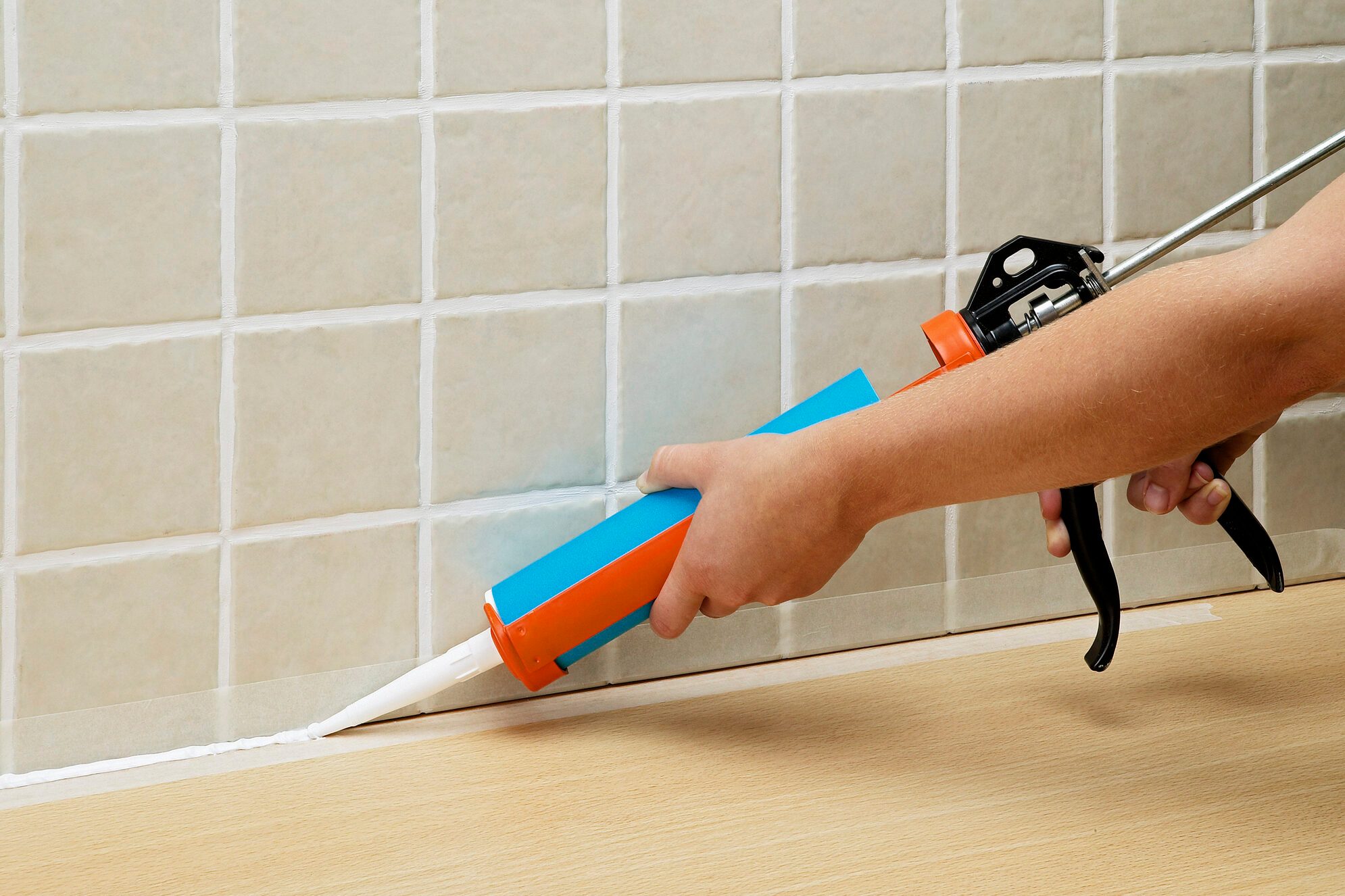 Hands applying sealant to tiles with sealant tube