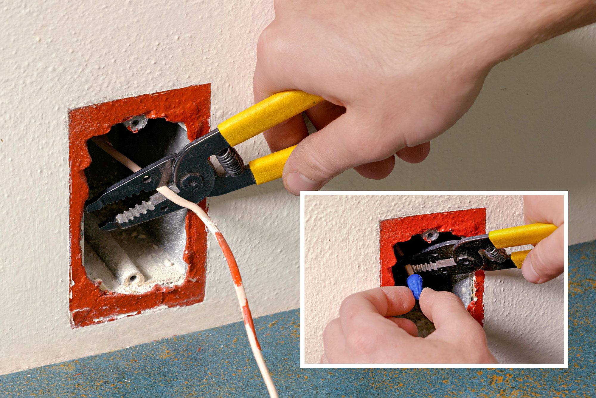 a close-up of a hand using a yellow and black handled saw to cut into a square section of drywall, An orange cable runs through the middle of the cut section, The wall is painted off-white with a visible texture, Below the square opening, there’s a round hole in the floor with a similar orange cable coming out;