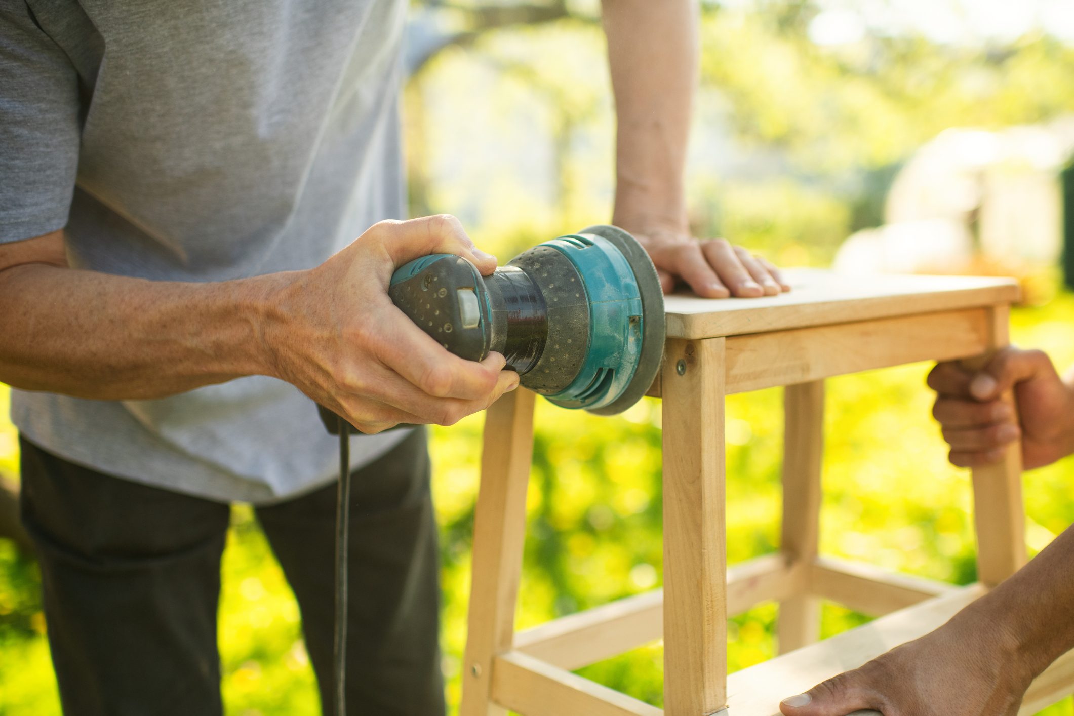 Senior man sanding a chair outdoors at back yard in sunny evening. Old furniture renovation. Sustainability concept.