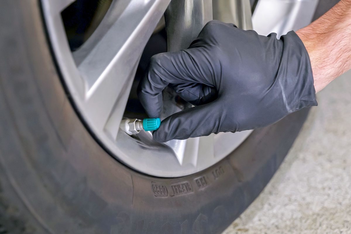 a closeup view of a person holding the tire valve stem cap in place; A person wearing a black glove; the tire is close to the ground; the person's arm is visible as well as some of their hand