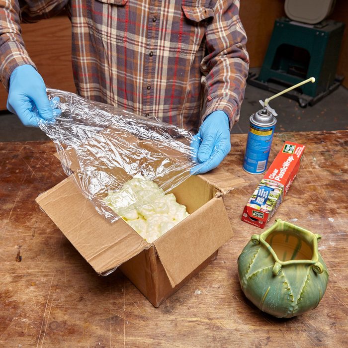 man holding plastic wrap over cardboard box filled third of the way with foam