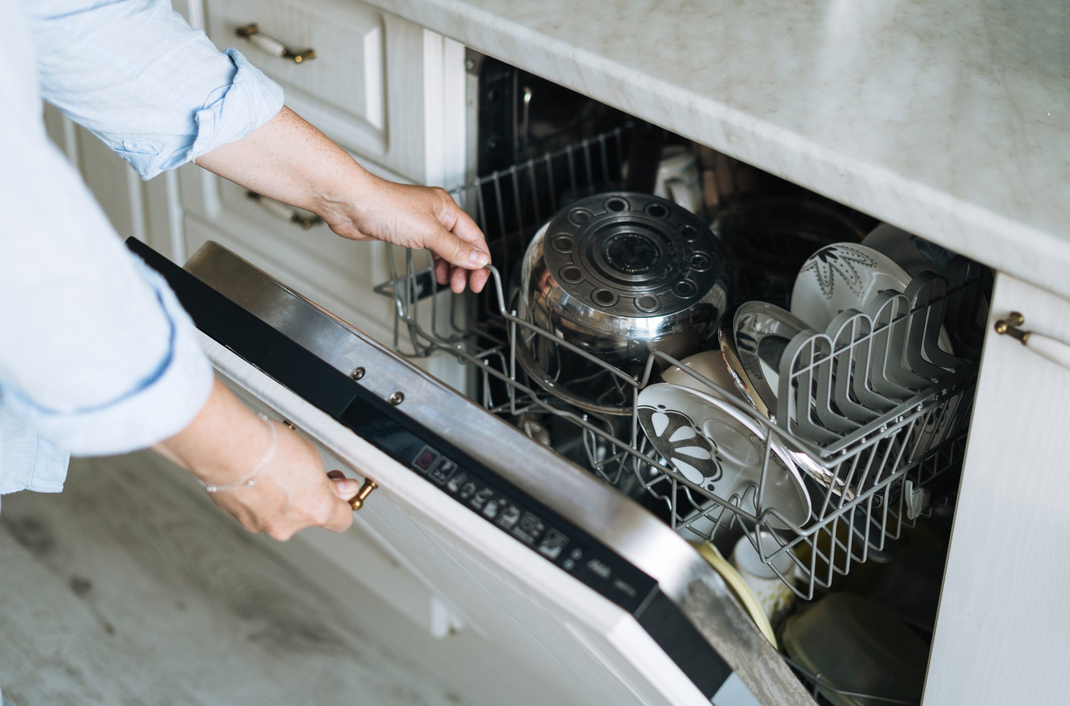 Adult woman in blue shirt using dishwasher at home
