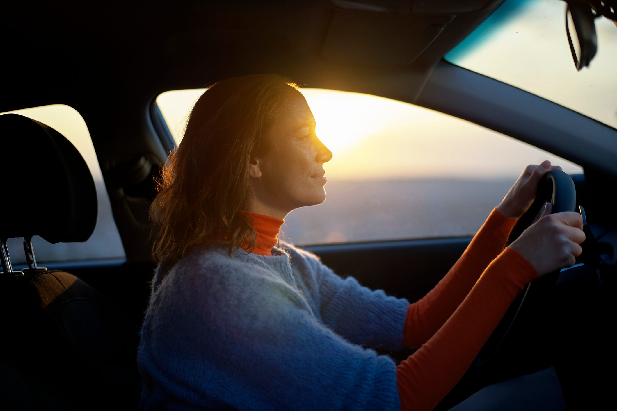 Woman driving a car during sunset with warm light on her face