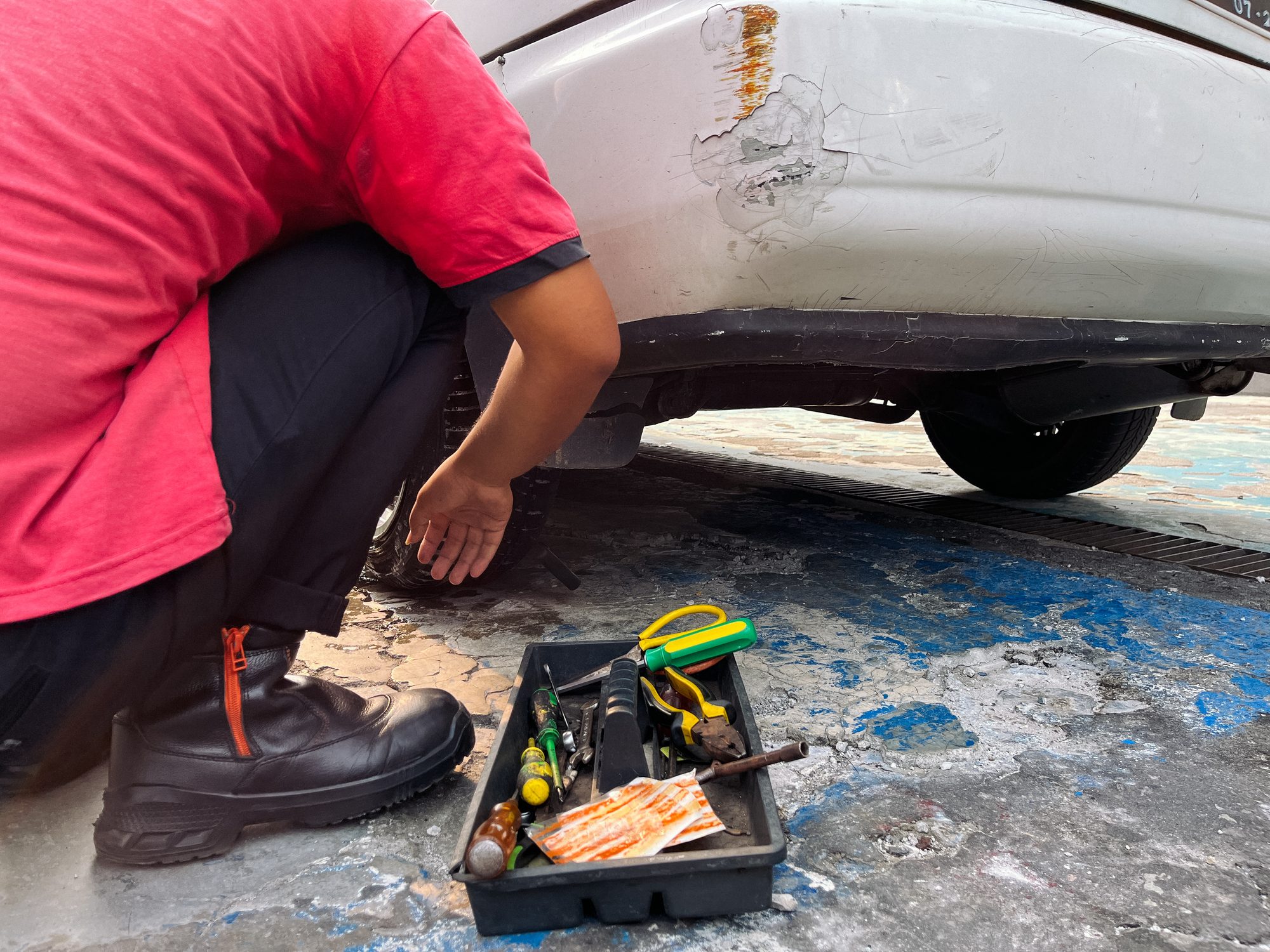 Man Checking Air Pressure in Car Tire with toolbox in front