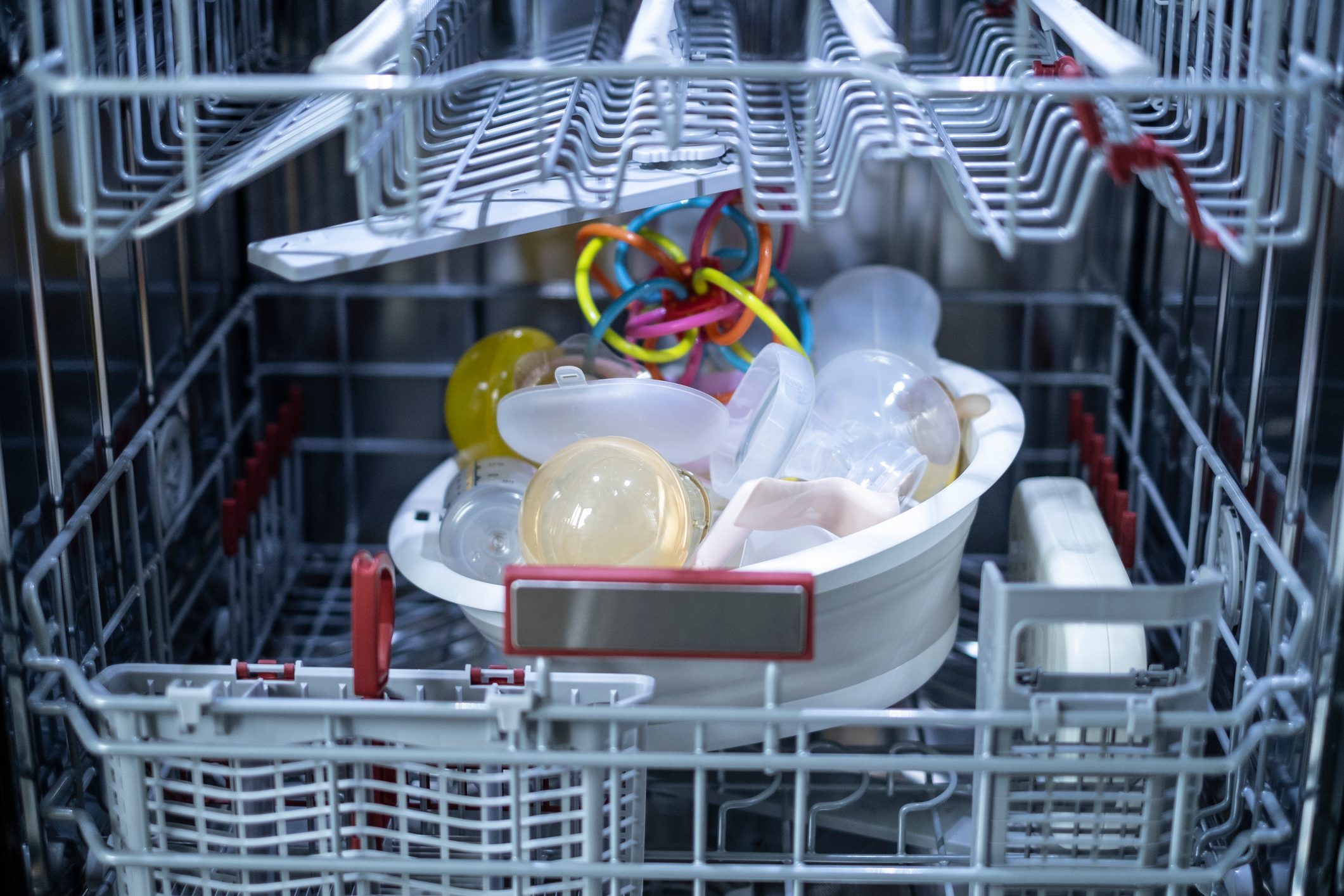 Baby toys and gear in the bottom shelf of a dishwasher