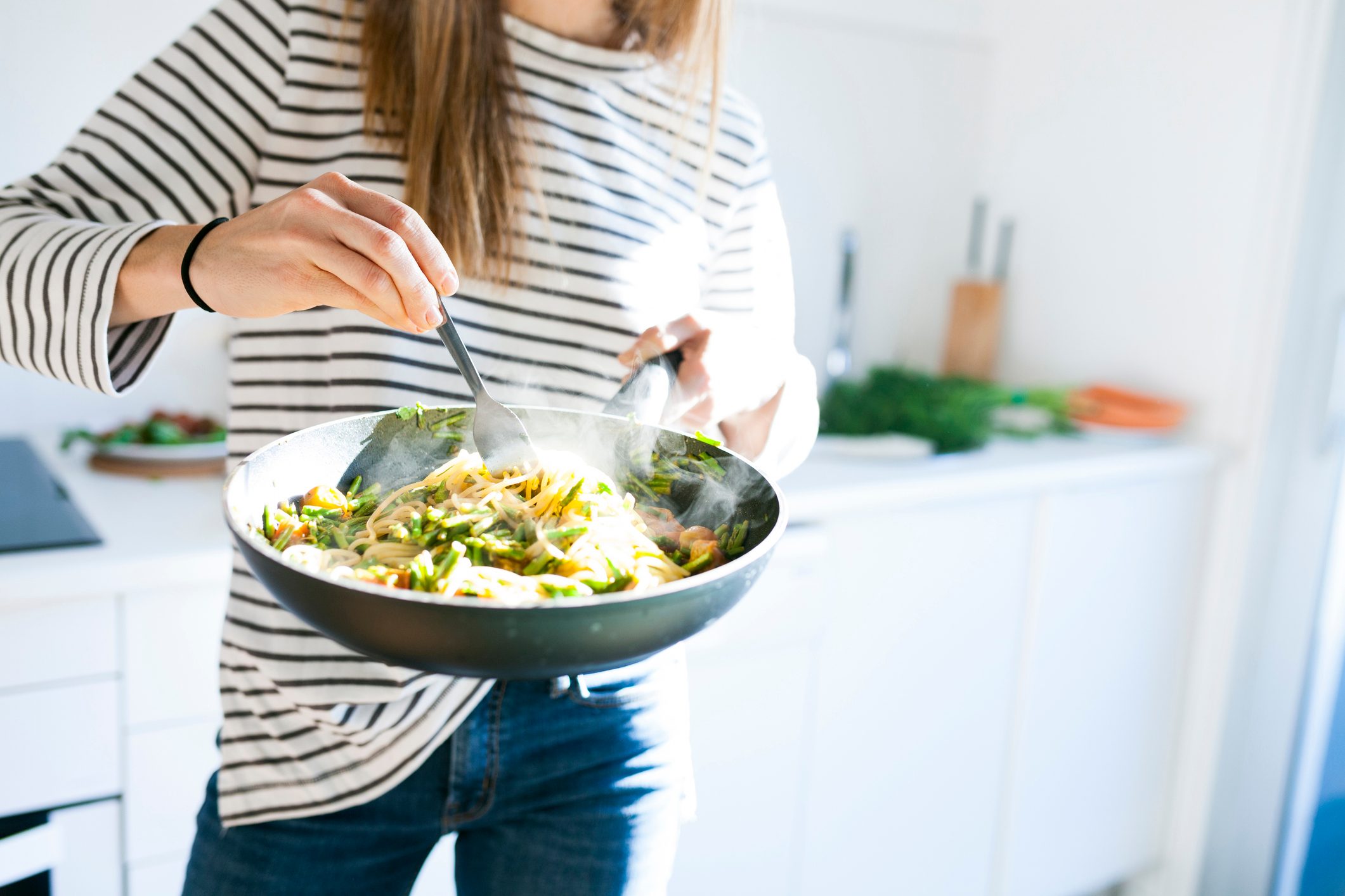 Woman holding pan with a steaming pasta and vegetable dish