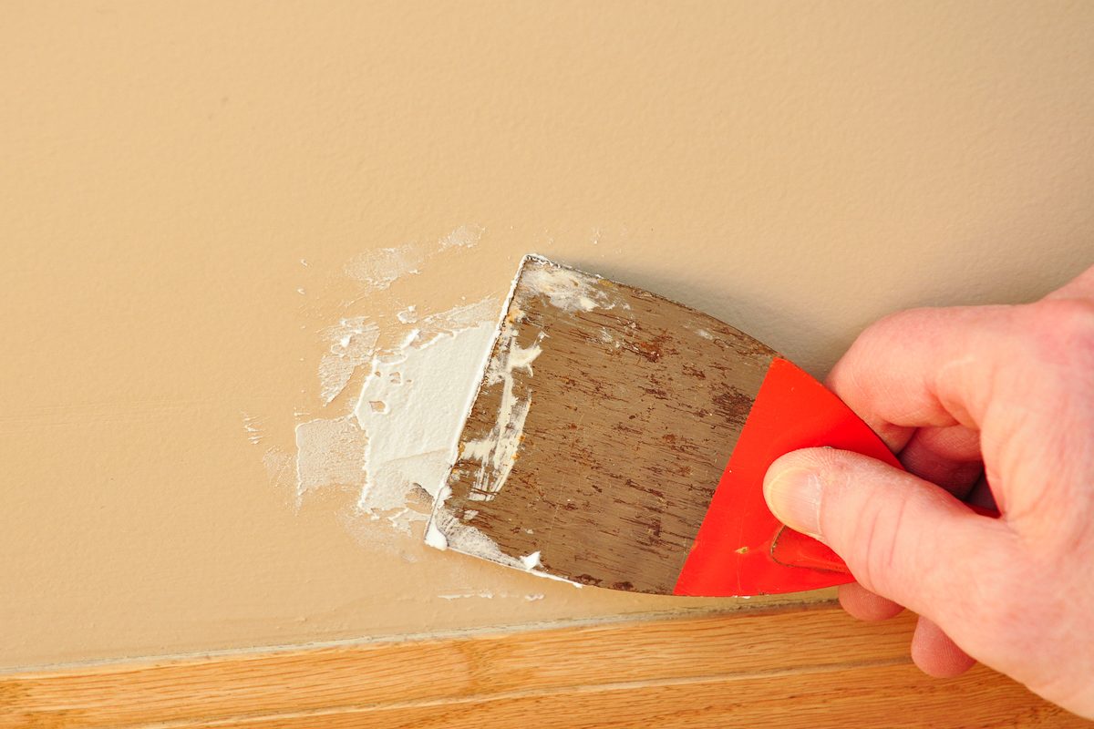 person using putty knife with spackling paste