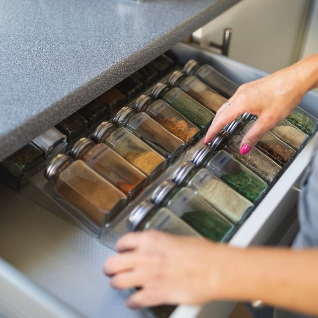 Hands of woman arranging spice jars in kitchen drawer