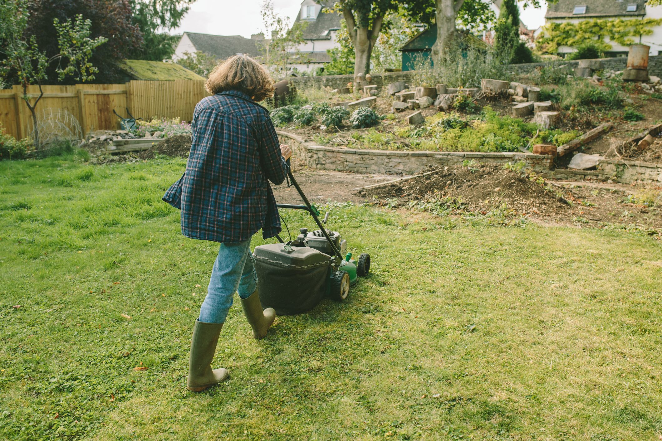 Senior Woman Mowing the Lawn in a Rustic Garden Setting