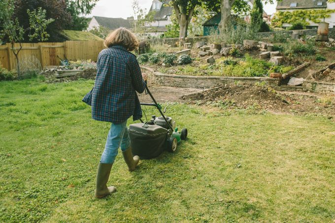 Senior Woman Mowing the Lawn in a Rustic Garden Setting