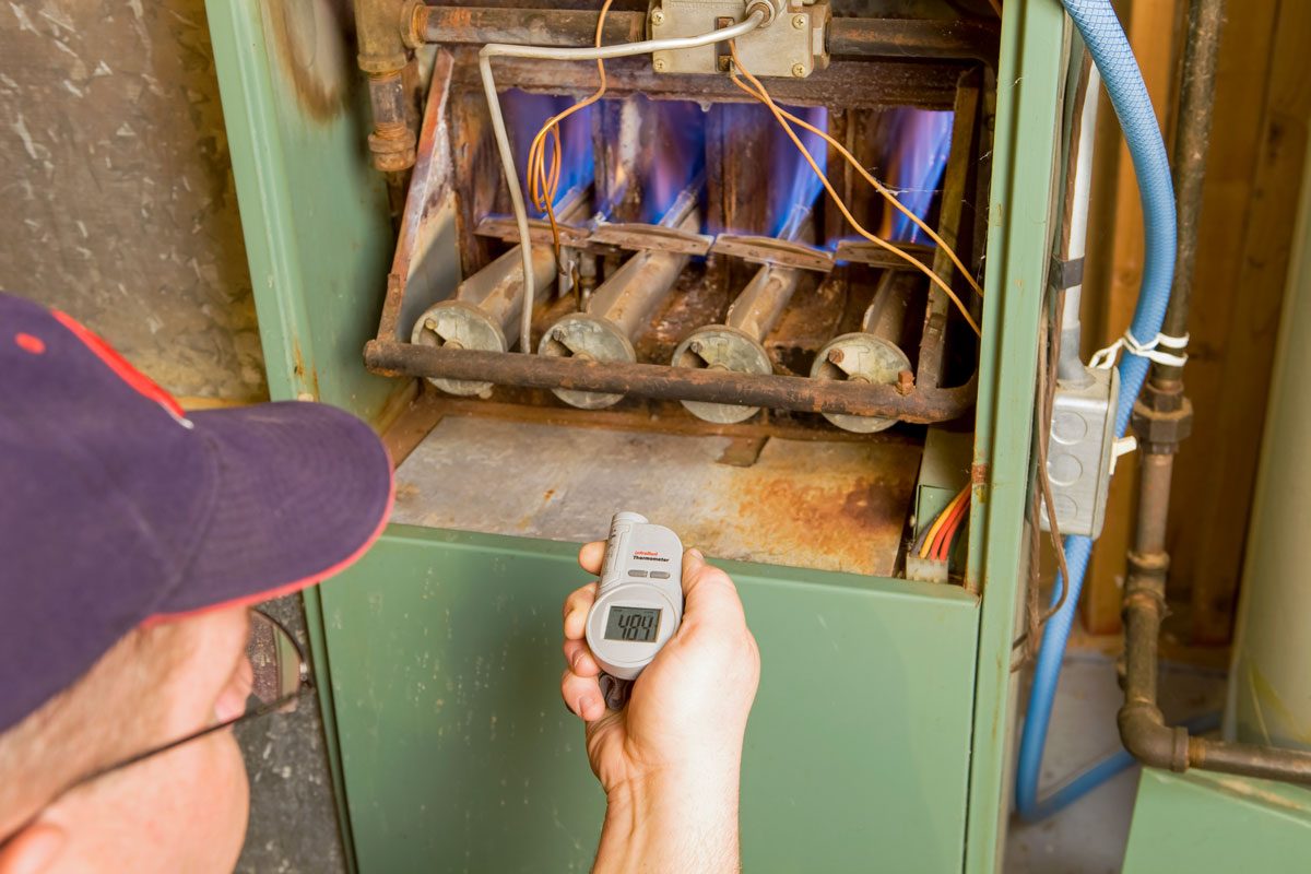 Repairman With Digital Infrared Thermometer Checks Gas Furnace Output Temperature