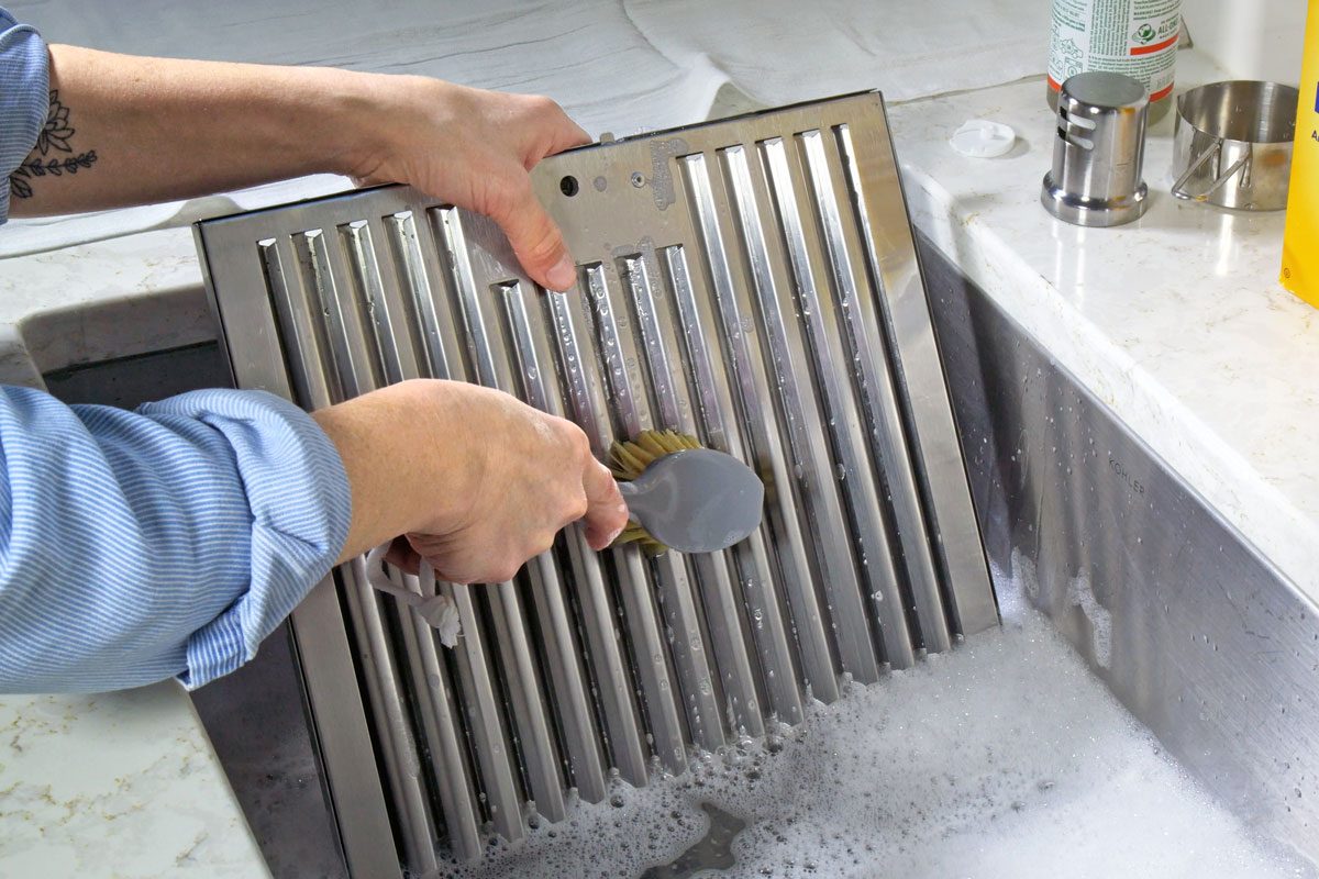 Use a scrub brush Scrub the filter with a scrub brush or sponge--using the mixture in the tub. Add Sal Subs directly to the brush to help the degreaser get into the cervices. Rinse with clean water. If more work needs to be done, drain and refill the sink with the mixture and soak for another 15 minutes. Still: Scrubbing filter 1. Fill the sink with hot water. If need be, boil some water and add it to the sink water so it is nice and hot. 2. Put 2-4 squirts of Sals Suds into the water 3. Add ½ cup of baking soda 4. Stir until baking soda is dissolved Still: Pouring Sal Suds into water