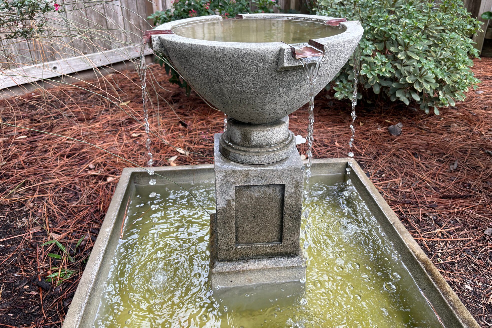 Cast Concrete water fountain with water flowing and pine needles in the background