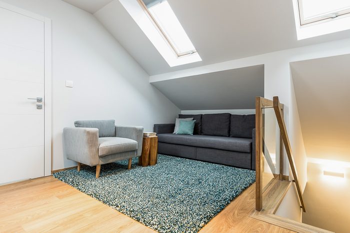 Comfortable gray armchair and black sofa in a relax corner of a white attic house interior with roof windows
