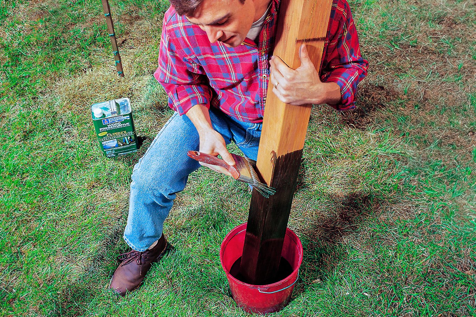 A person applying a black coating to a cedar fence post