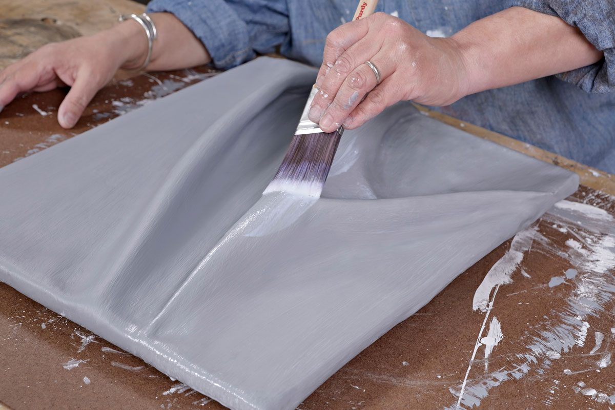 a hand is seen applying a coat of light gray paint to a textured surface using a paintbrush;