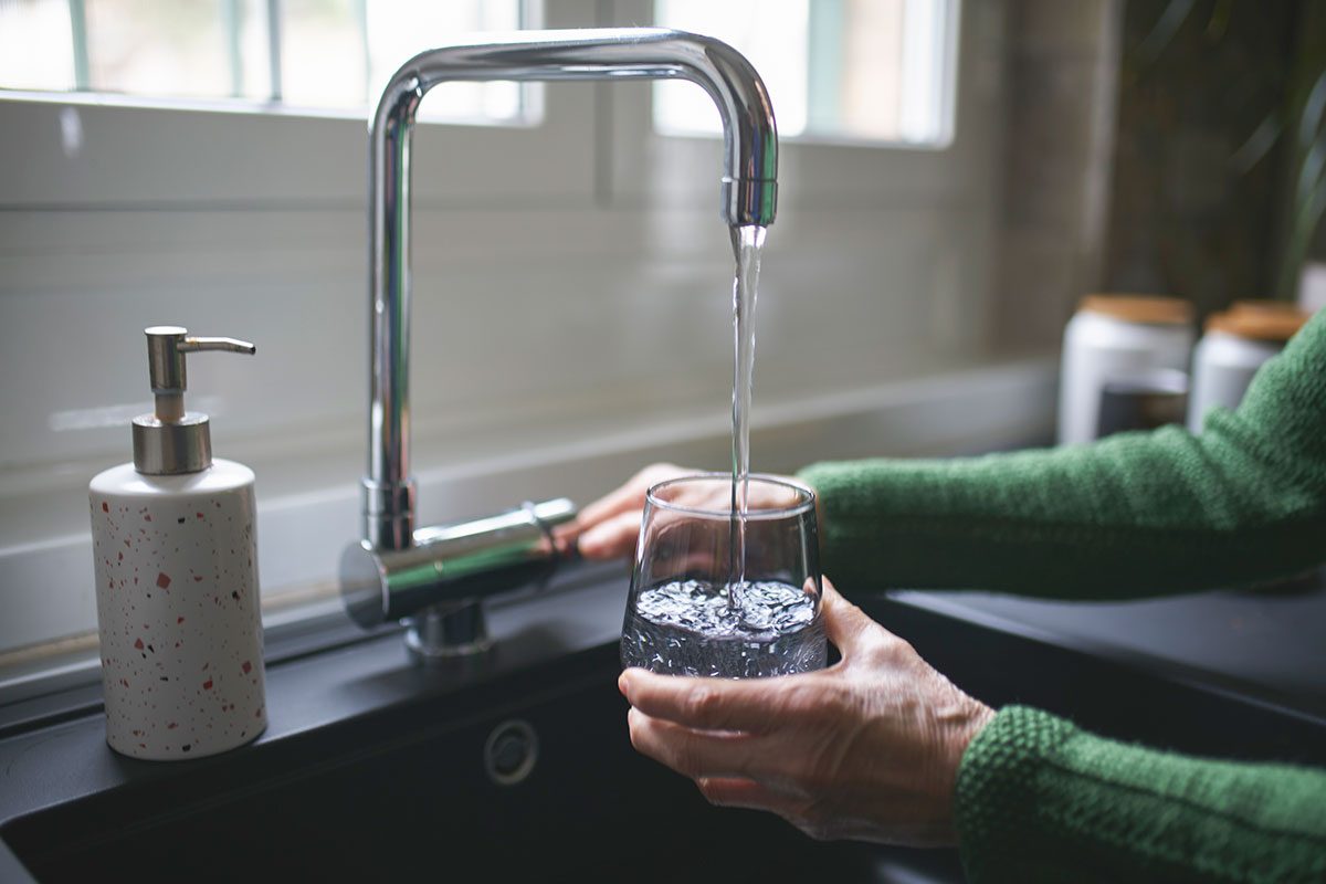 Close up of a senior woman's hand filling a glass of filtered water right from the tap in the kitchen sink