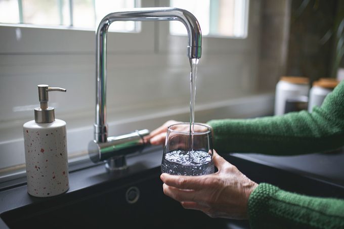 Close up of a senior woman's hand filling a glass of filtered water right from the tap in the kitchen sink