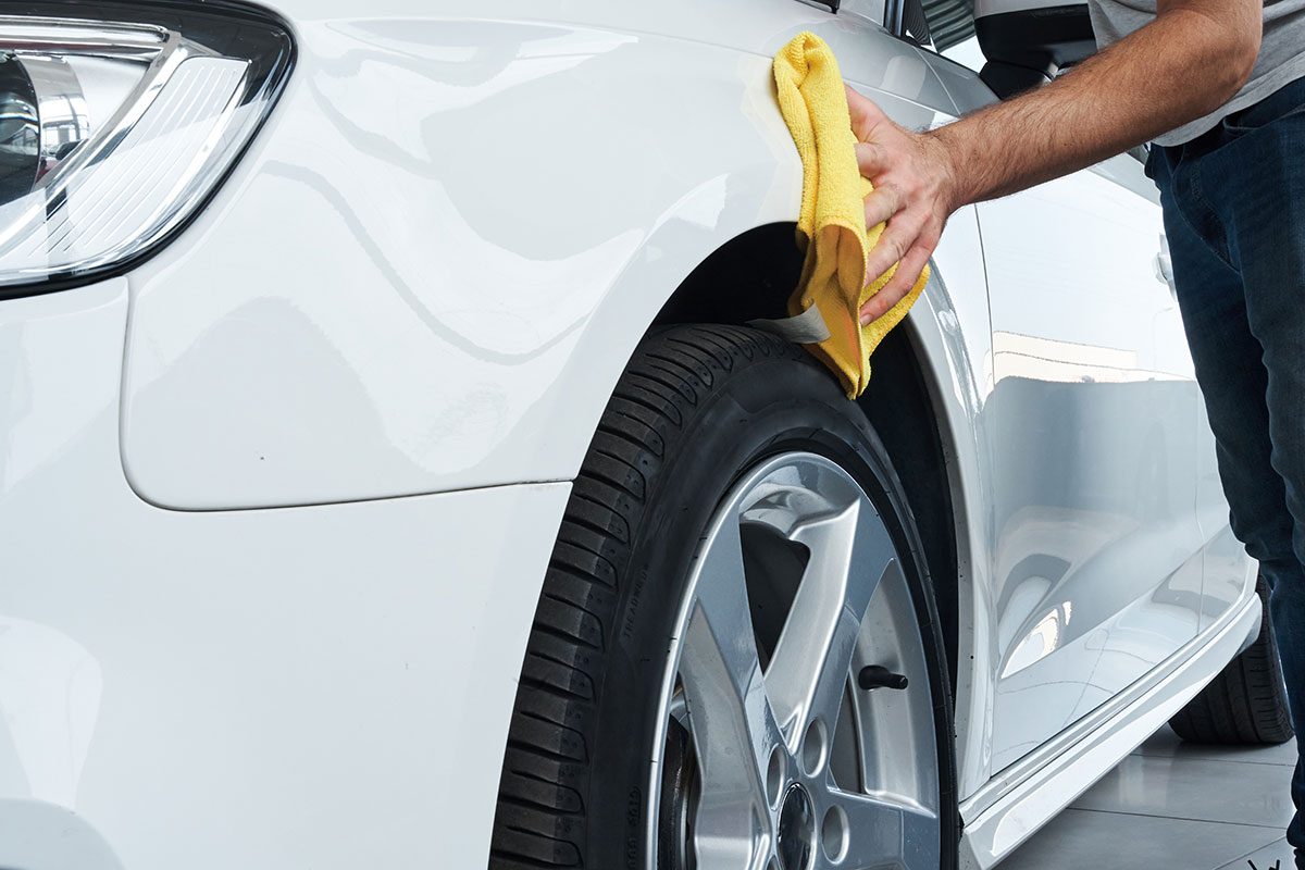 Close up view of a worker detailing polishing a white car with a rag