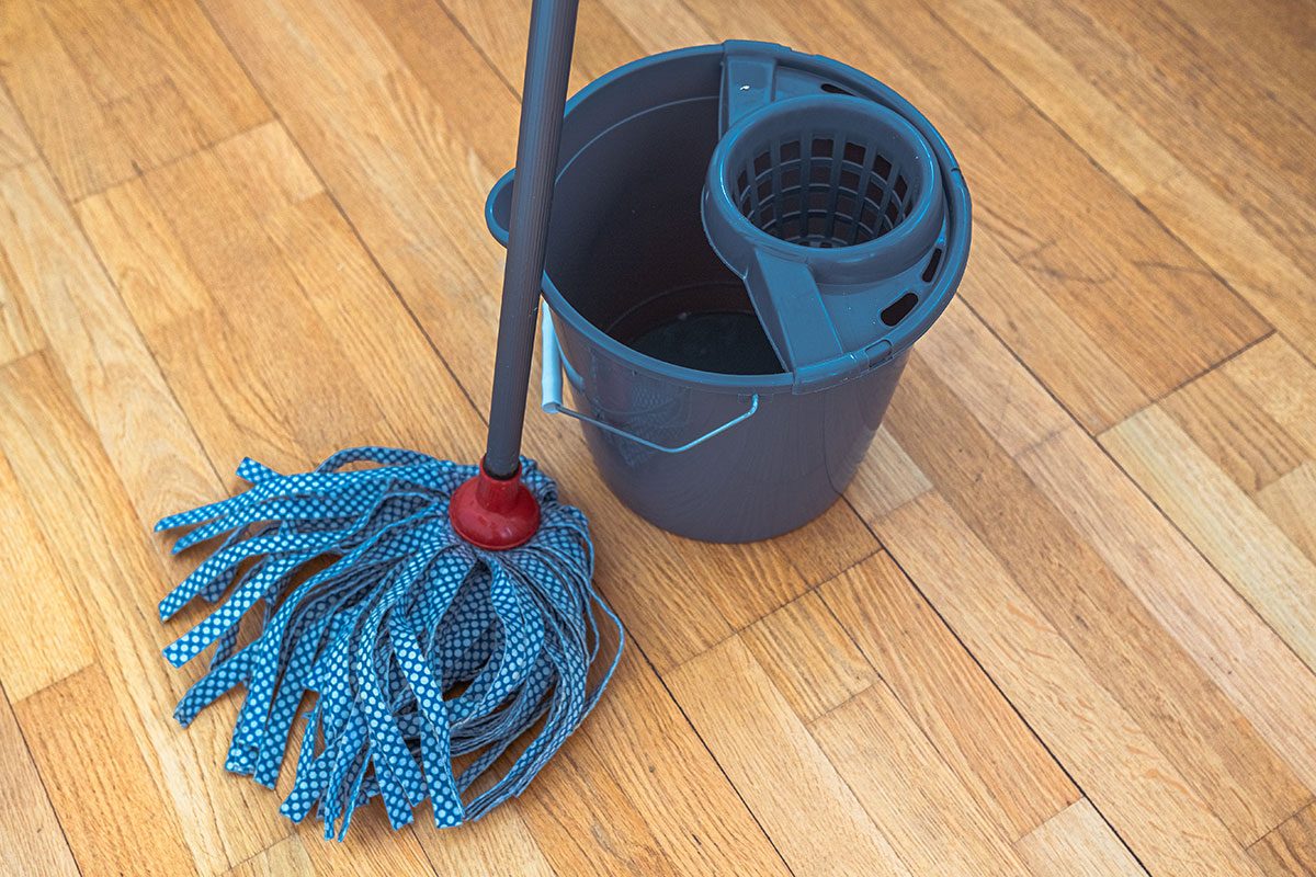 Mop with tape nozzle and bucket for mopping floor with wring function on background of wood floor