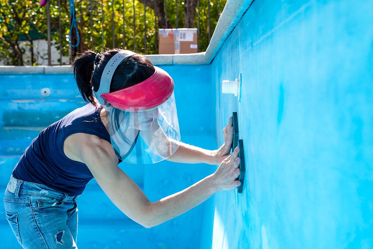 Woman with face protective mask sanding with a sponge the swimming pool.