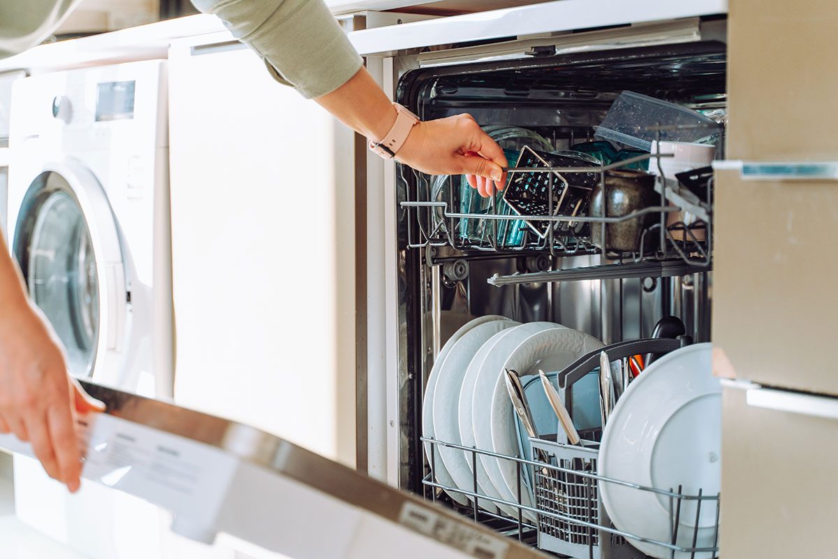 hands loading dish washing machine near washing machine in modern built in kitchen