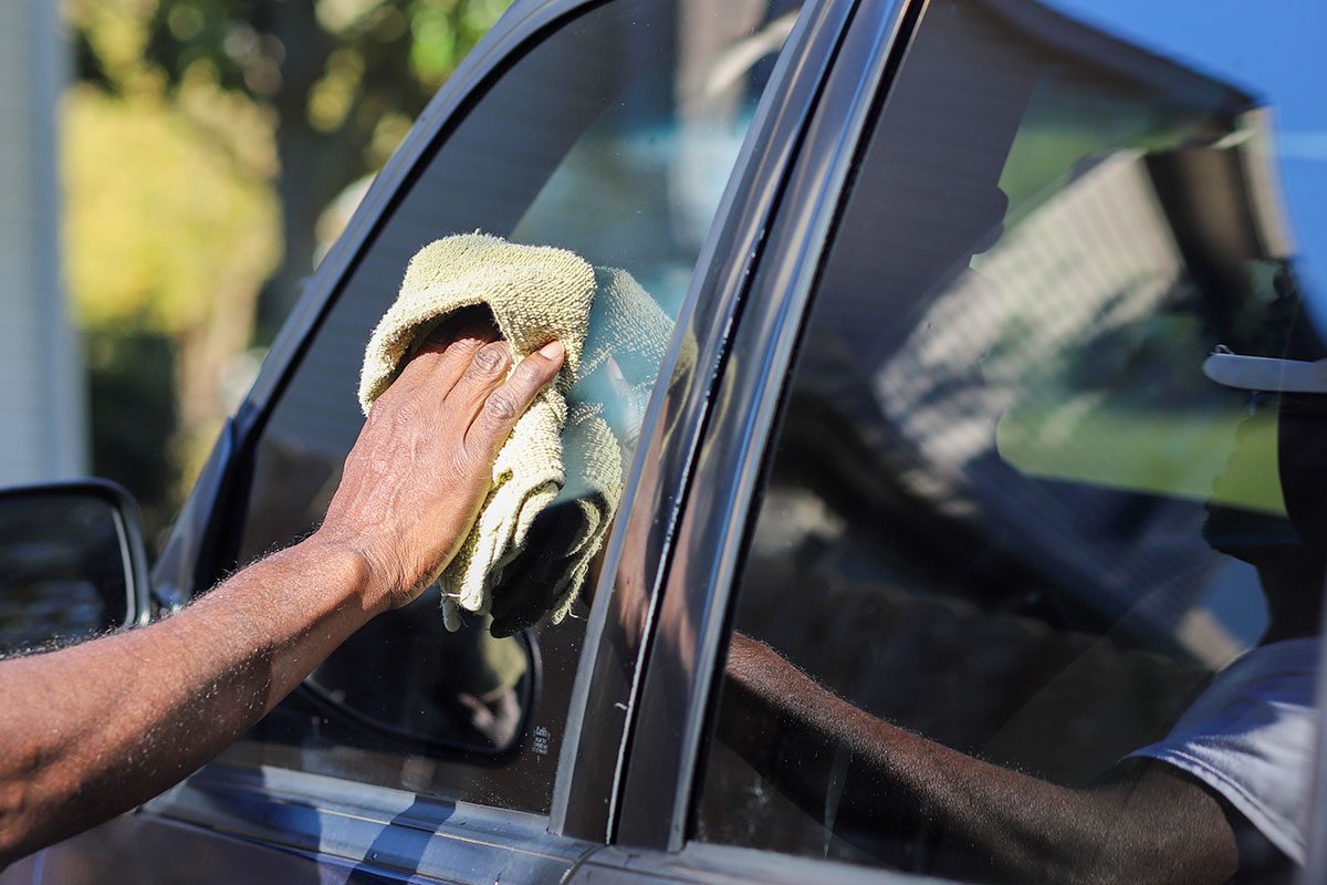 man cleaning a vehicle exterior glass window in the summer with a cloth