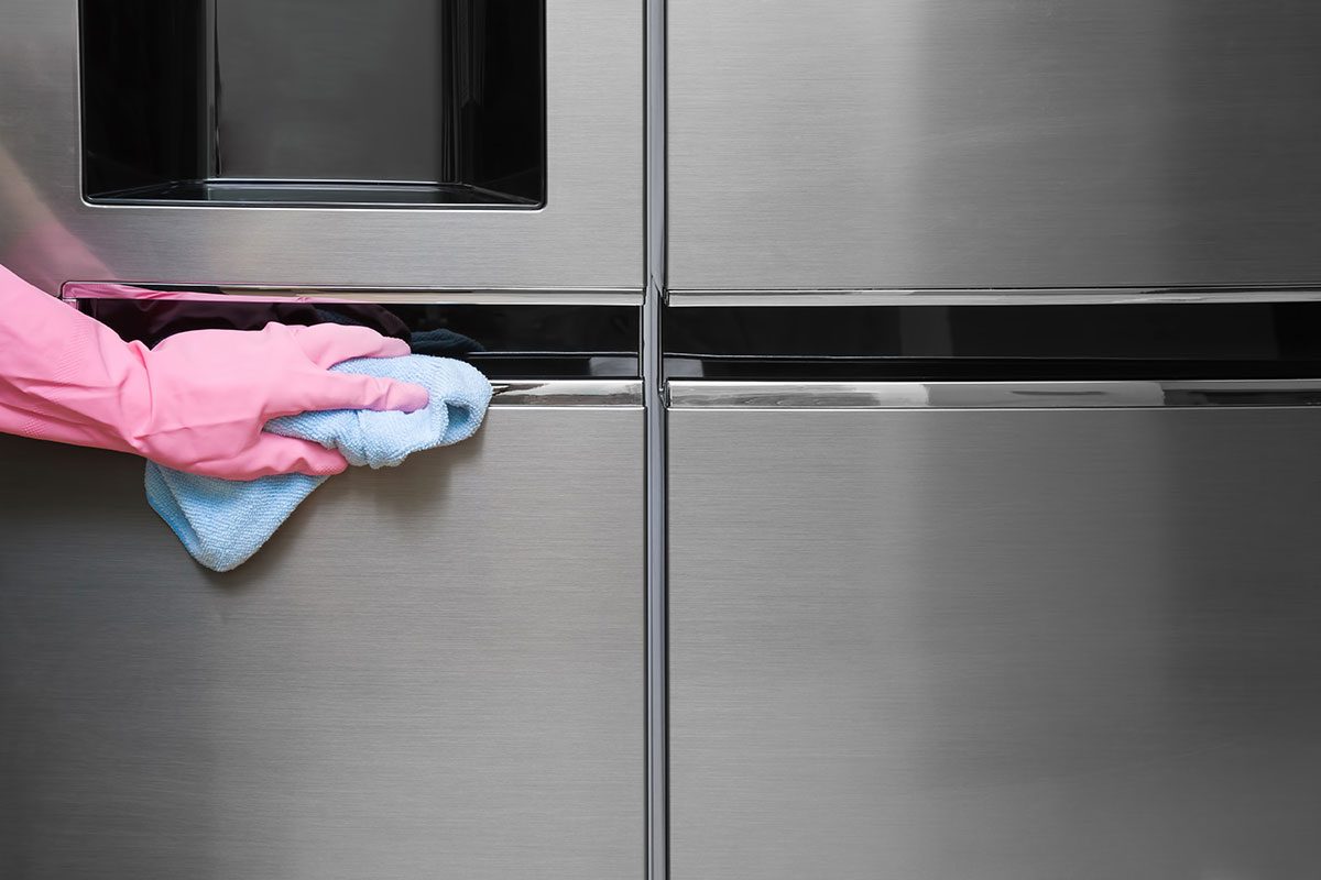 Employee hand in rubber protective glove with micro fiber cloth wiping a fridge