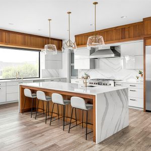 Beautiful kitchen in new luxury home with waterfall quartz island, pendant lights and hardwood floors