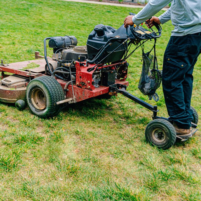 Expert Latino Man Using a Stand-On Lawnmower, Caring for a Park with a Landscaping Company