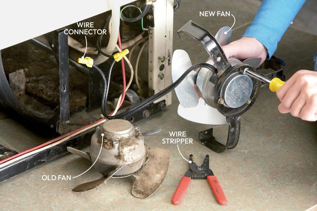 A technician installs a new fan beside an old, dusty fan, using a wire stripper on a countertop with visible electrical connections.