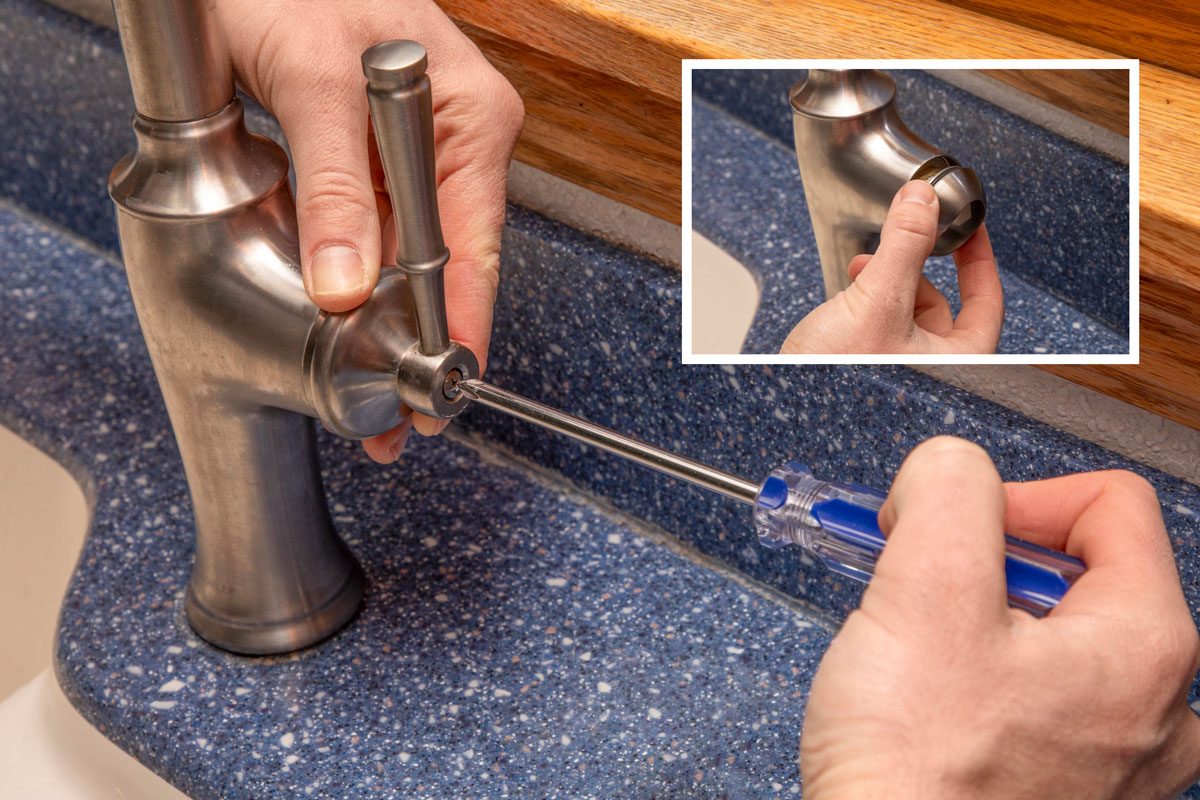 two hands using a screwdriver with a blue handle to tighten a screw on the side of a brushed metal kitchen faucet handle; the faucet is mounted on a blue speckled countertop, and a white sink is partially visible on the left; a wooden window sill is in the background; a hand inserting a shiny, round metal cap into the side of a brushed metal kitchen faucet; the faucet is mounted on a blue speckled countertop, and a white sink is partially visible on the left; a wooden window sill is in the background