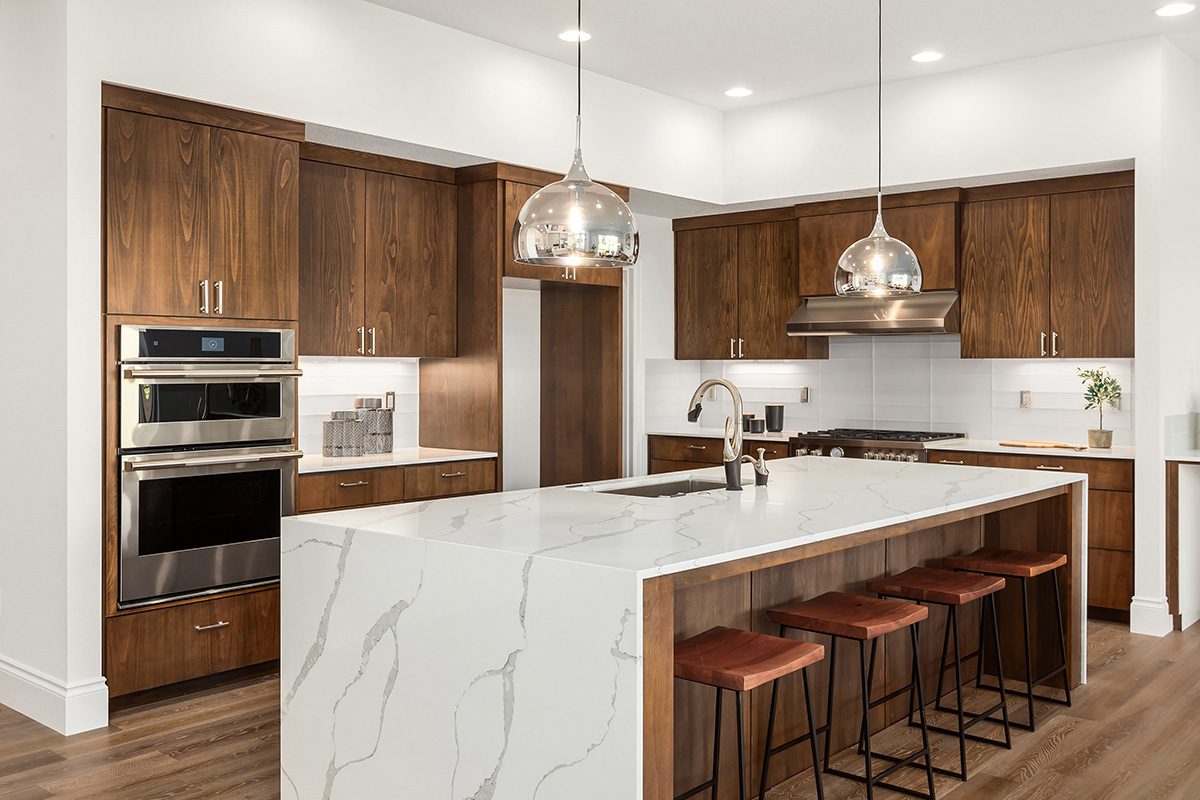 Beautiful kitchen in new luxury home with island, pendant lights, and hardwood floors. Features quartz waterfall island with dark cabinets and stainless steel appliances