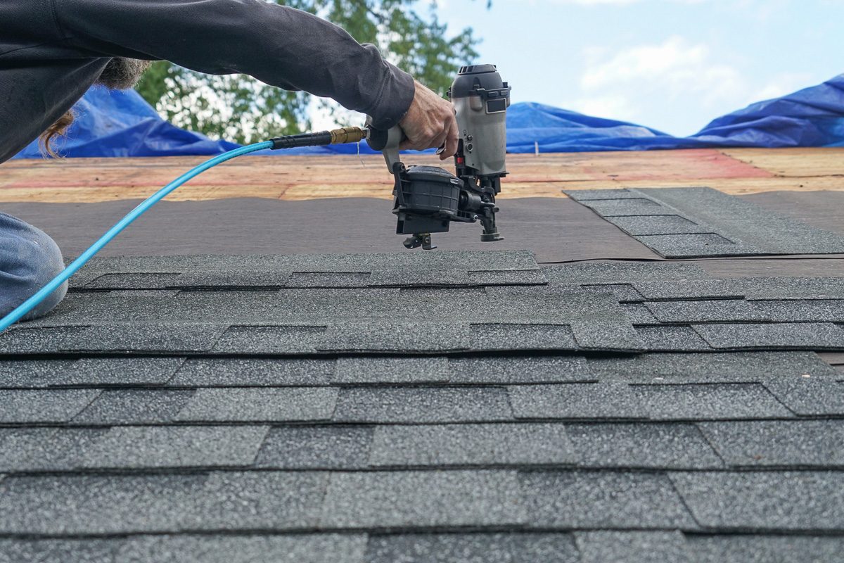 handyman using nail gun to repair roof shingles