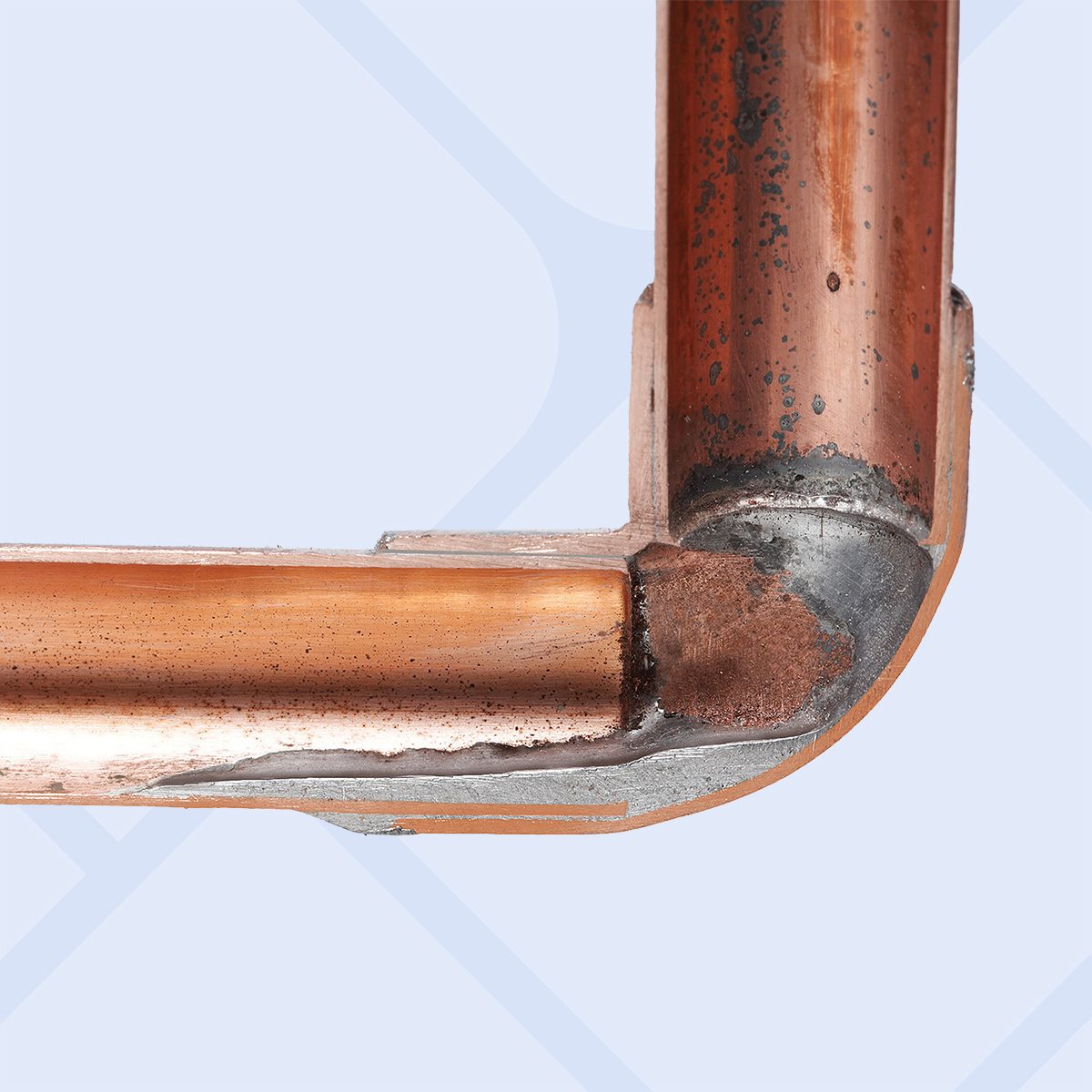 Close-up of two copper pipes joined at a right angle with a soldered elbow joint against a light blue background.