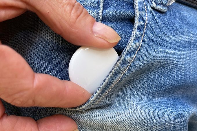 A hand keeping Apple AirTag in a jeans pocket