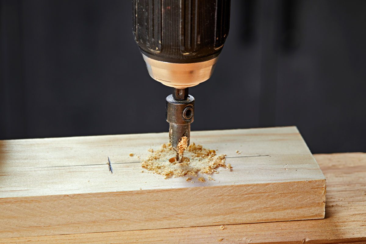 a close up view of a drill bit drilling into a piece of light colored wood;