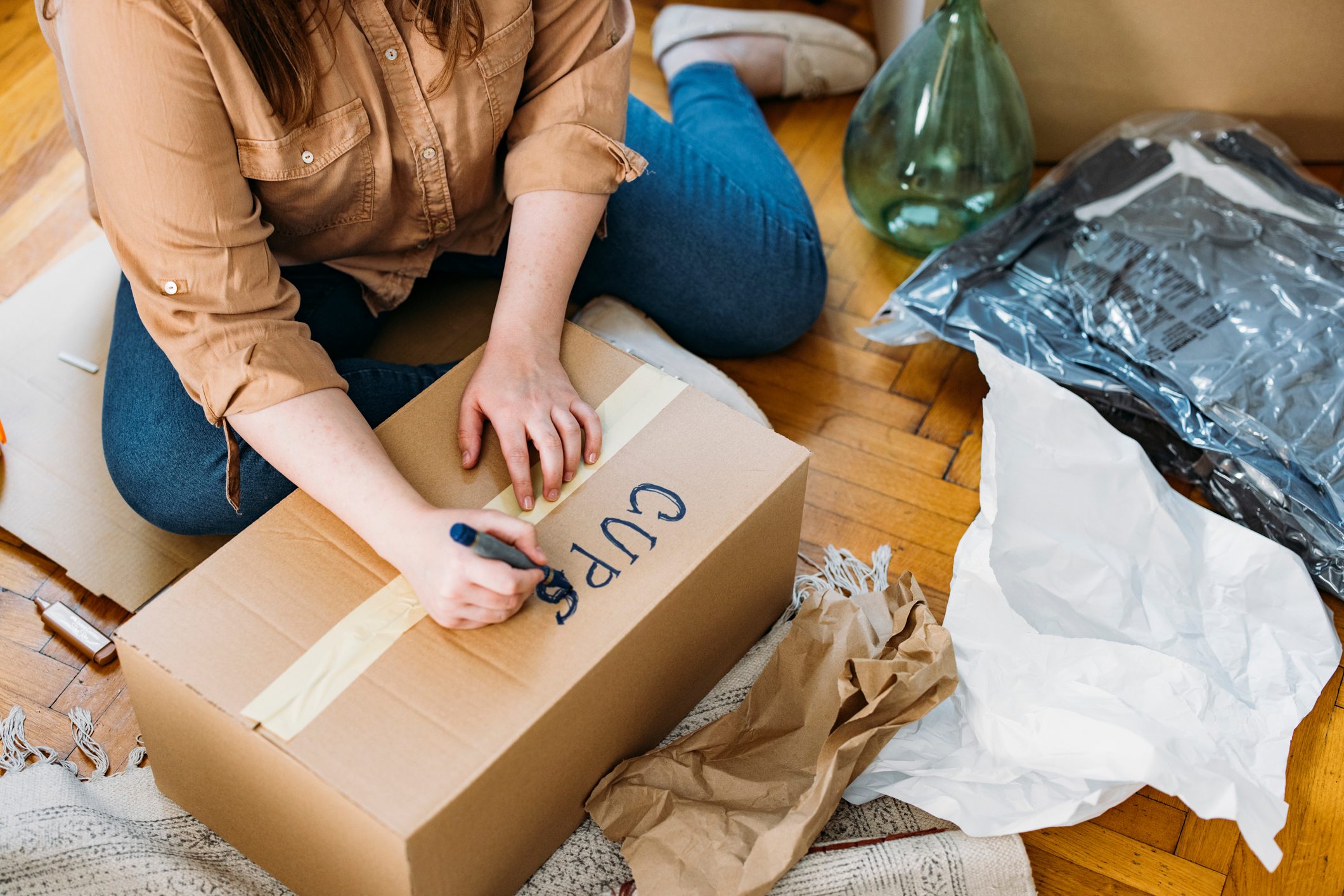 Moving out: Unrecognizable Plus Size Woman Sitting on the Floor while Labeling Packed up Cardboard Box, Horizontal Shot