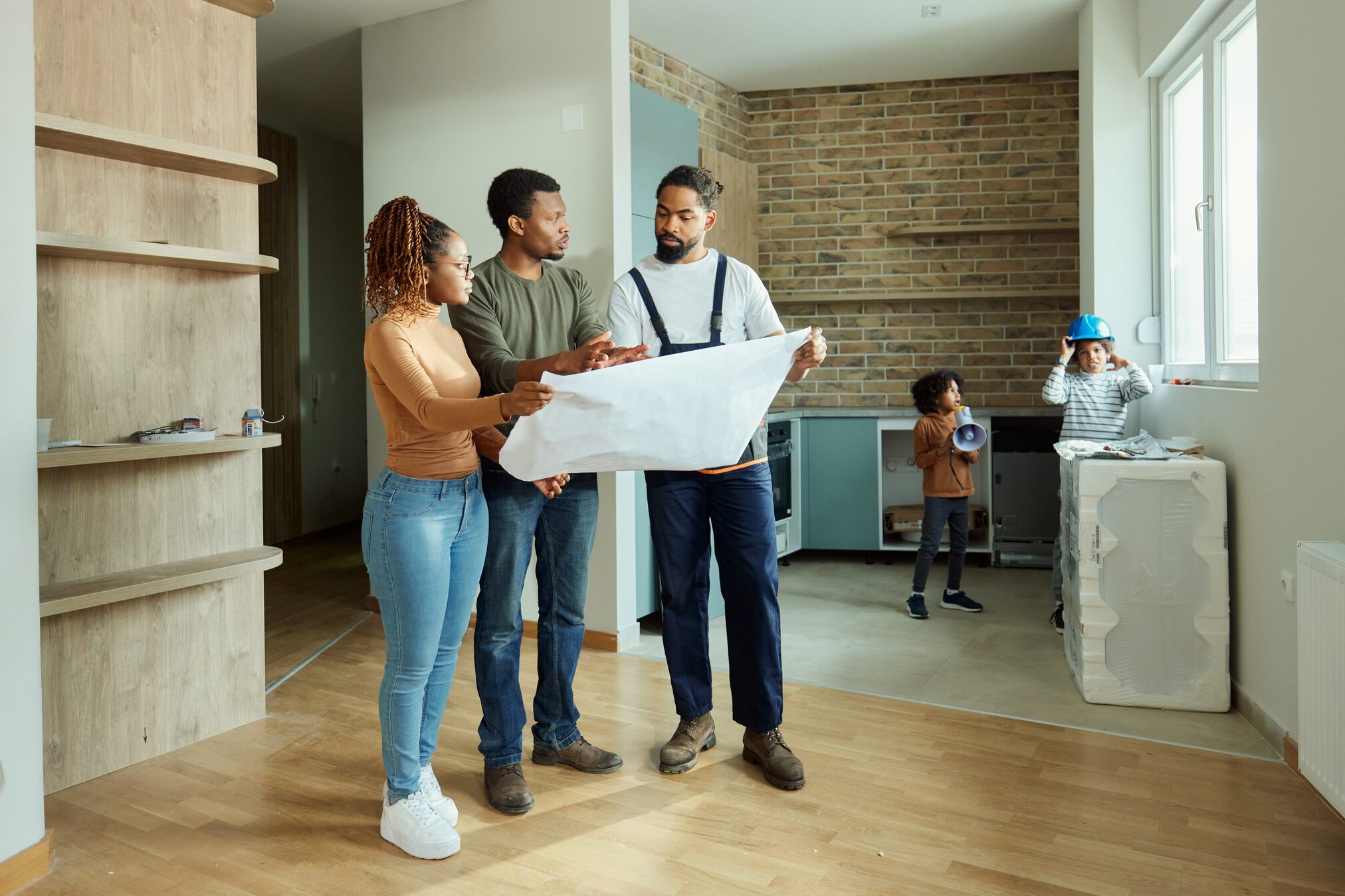 Black parents and manual worker analyzing blueprints in the apartment.