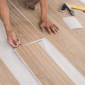 A technician is cutting luxury vinyl floor tiles with a cutter to lay the floor before placing it on the leveling foam.