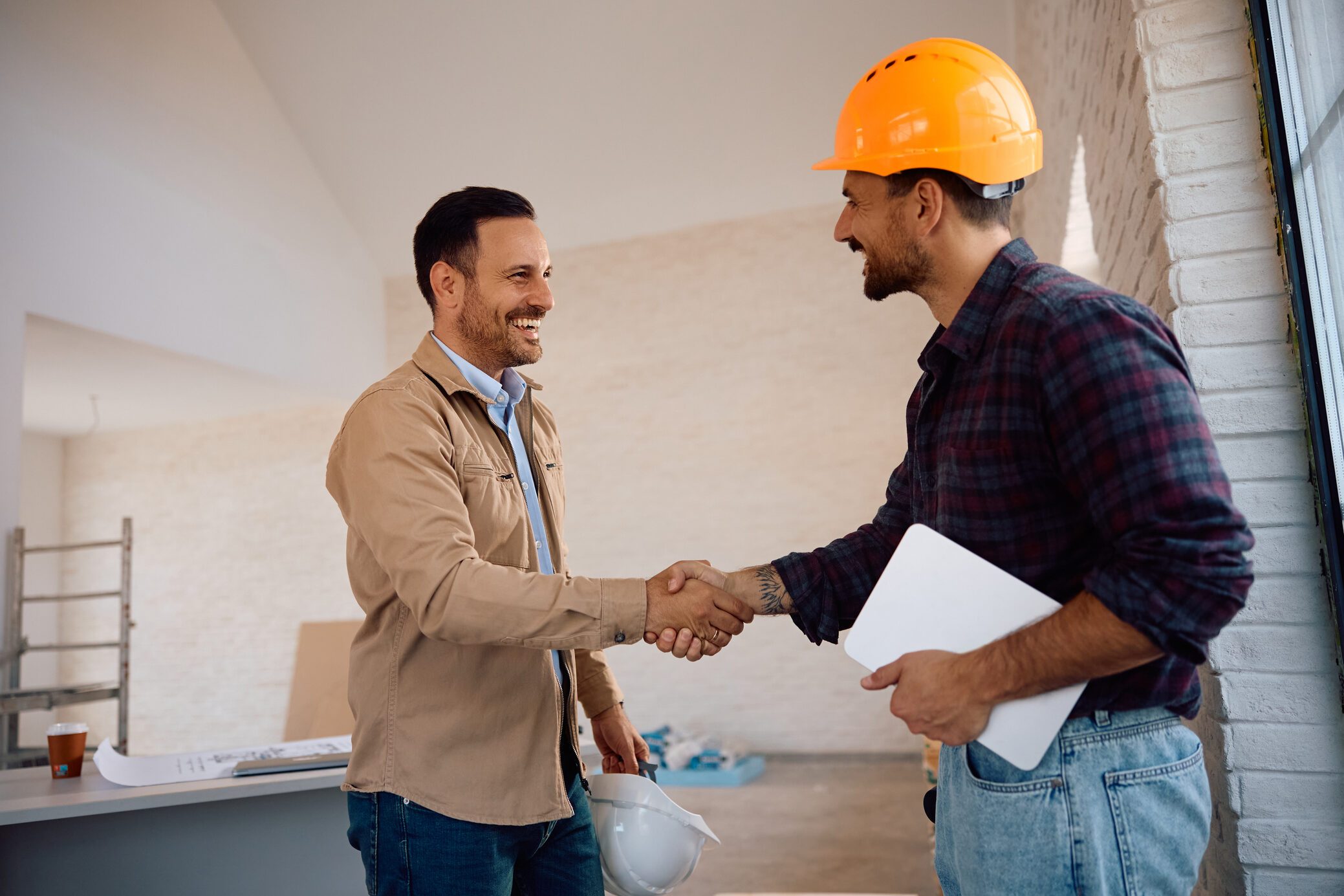 Happy home owner and construction site worker handshaking at renovating house.