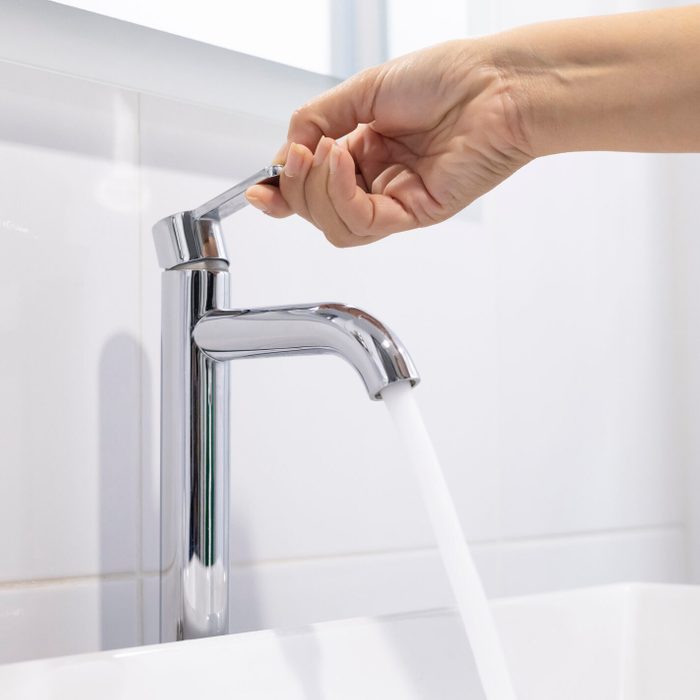 close up Woman open pull chrome faucet washbasin to washing hand soap for corona virus at water tap. push off water running drop off. Bathroom interior background with sink basin faucet tap.