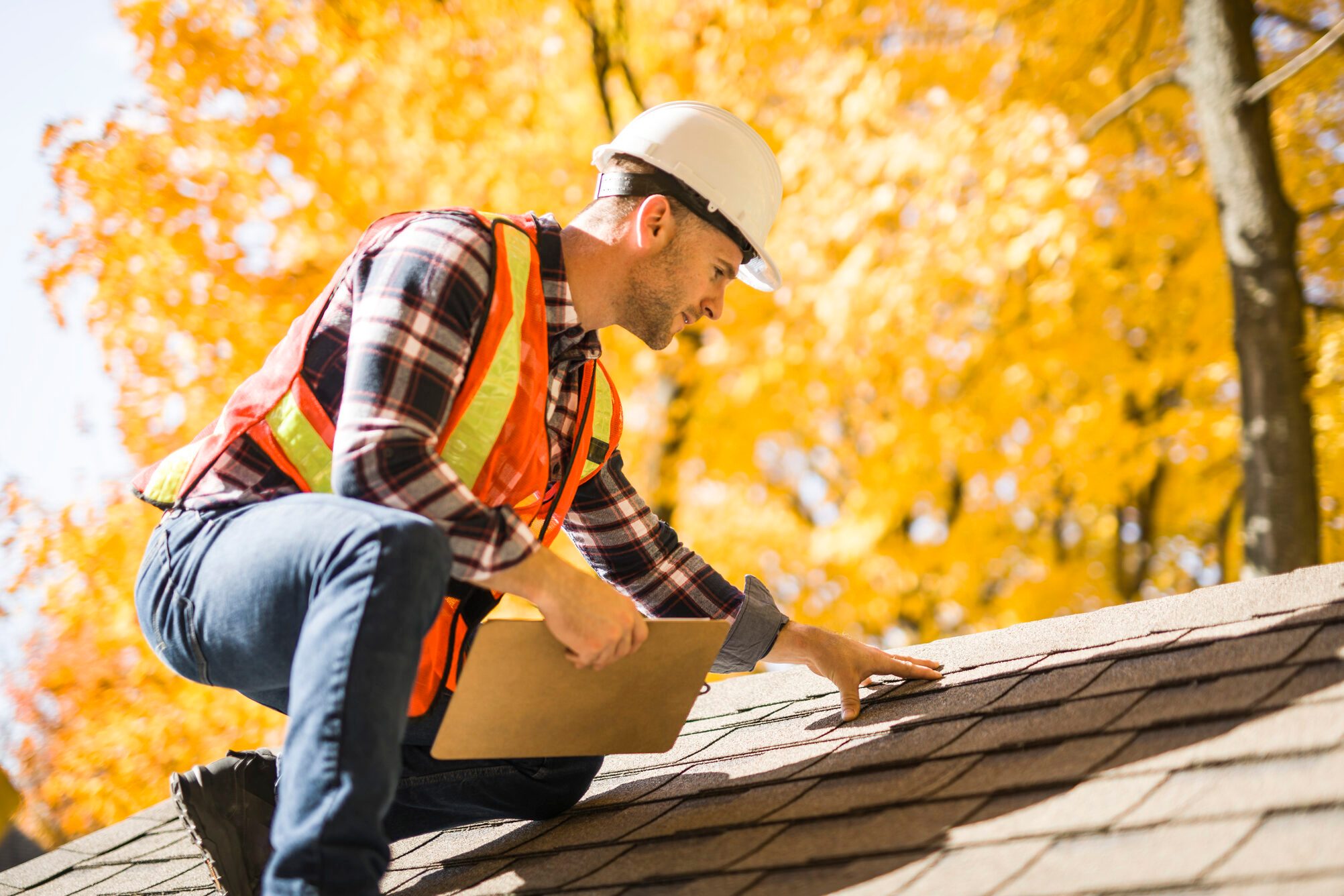 man with hard hat standing on steps inspecting house roof