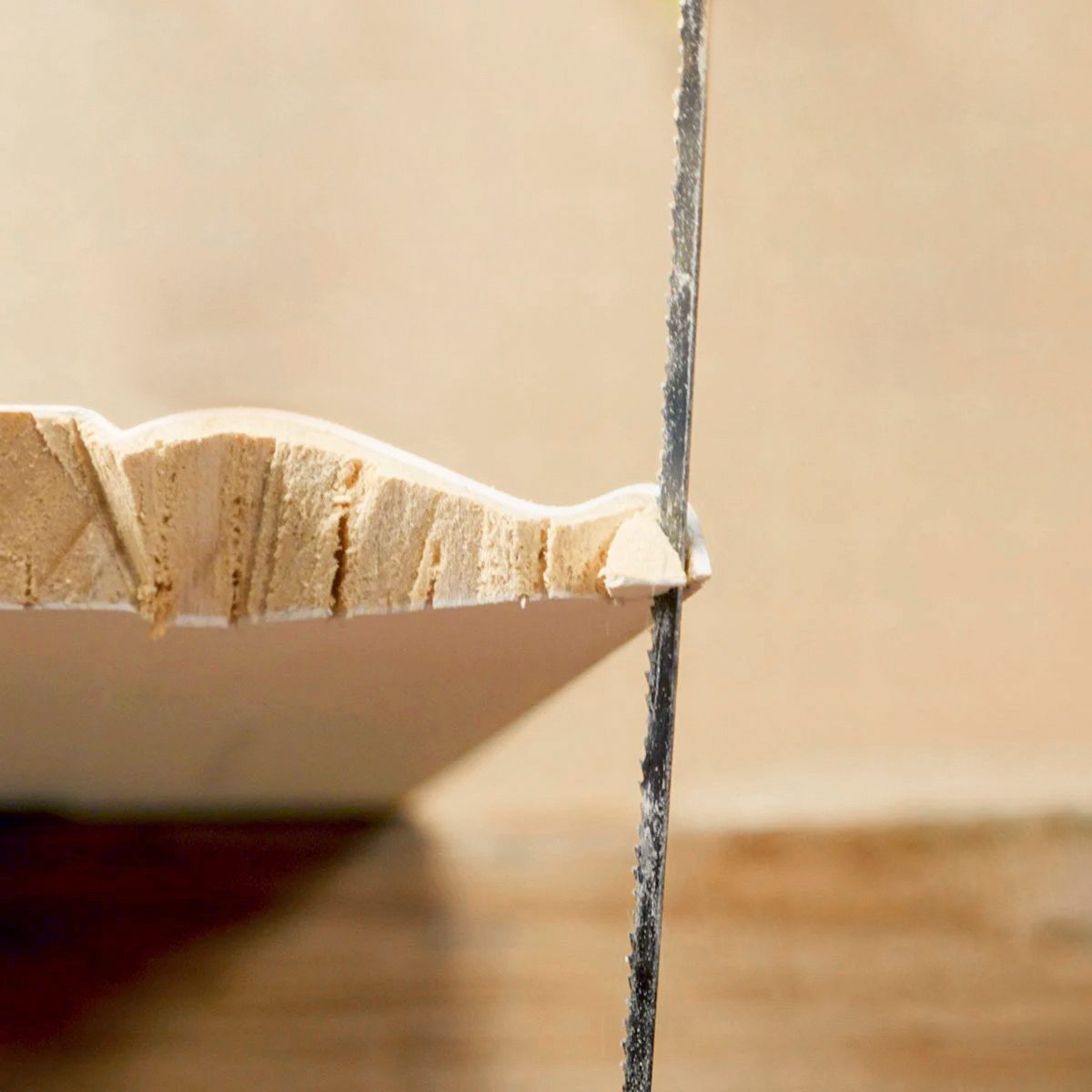 A close-up of a saw cutting through a piece of wood, with wood shavings visible along the edge of the cut.