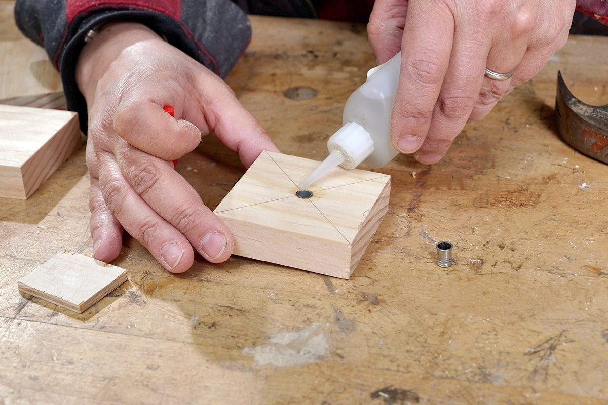 A person applies glue to the hole in the center of a small wooden block while holding it on a workbench.